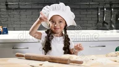 小可爱的女孩假装厨师戴着厨师帽，在<strong>厨房</strong>里用<strong>擀面杖</strong>做小块面团。 玩得开心